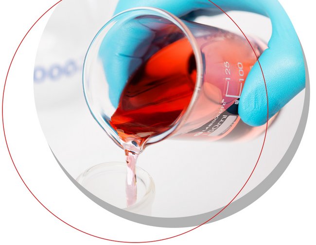 Laborbecher mit roter Flüssigkeit wird von Hand mit Handschuh in Glasgefäß gegossen