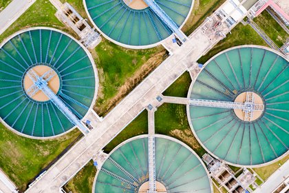 Luftaufnahme einer modernen Kläranlage mit mehreren kreisförmigen Becken zur Wasseraufbereitung.